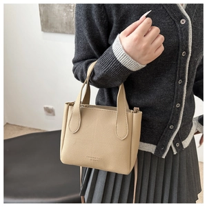 Détail du sac seau en cuir litchi beige avec logo gaufré et doubles poignées rondes
