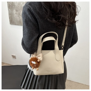 Detail of beige lychee leather bucket bag with fashion lettering and cute monster plush charm