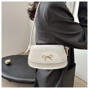 Detail of white glossy shoulder bag with a gold bow clasp and knotted strap detail