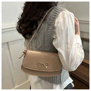 Détail d'un sac sous le bras beige avec un nœud doré sur une tenue de mannequin décontractée