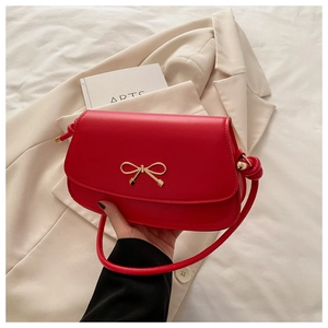 Détail d'un sac carré en cuir rouge avec fermoir nœud doré et bandoulière à nœuds