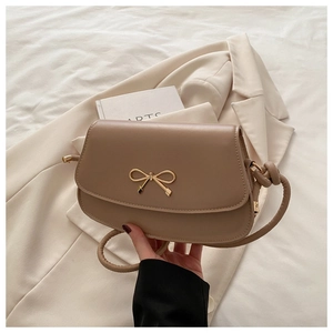 Détail du sac selle chameau avec boucle nœud doré sur un blazer beige chic