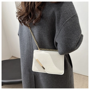 Chic white patent leather crossbody bag with gold chain strap on grey coat model