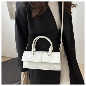 Detail view of white minimalist handbag with gold hardware and adjustable strap on a coat