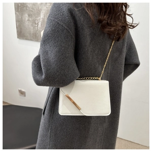 Close-up of cream rectangular crossbody bag with gold chain strap on a grey coat