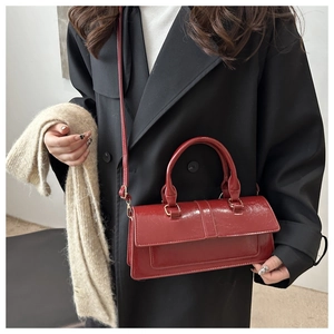 Detail of dark red patent leather baguette bag with a crackle texture on black coat