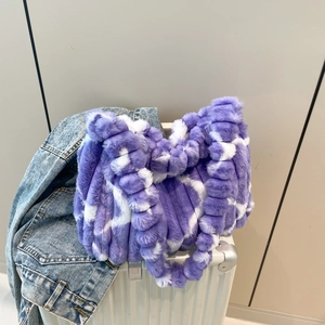 Purple and white plush faux fur tote bag resting on a white suitcase in a travel setting