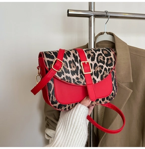 Detail of red leather crossbody bag with leopard print flap and golden metal buckle