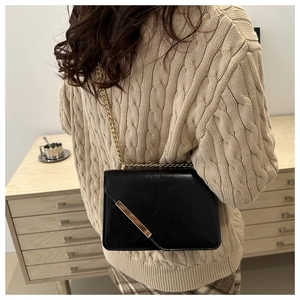 Detail of a chic black crossbody bag with gold chain strap worn over a beige sweater