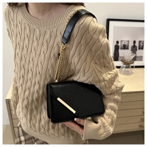 Detail of a black crossbody bag with gold metal trim and chain strap on a knit sweater