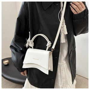 Close-up of white leather handbag with gold letters and decorative rope handle on model