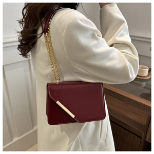 Detail of burgundy envelope crossbody bag with asymmetric flap and gold chain strap