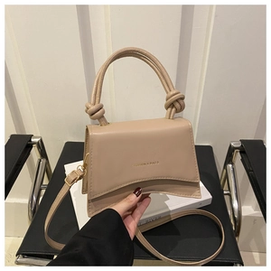 Detail of beige leather crossbody bag with knot handles and gold lettering on prop
