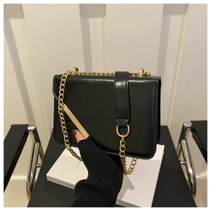 Detail of a black glossy chain shoulder bag featuring gold hardware and a D-ring strap