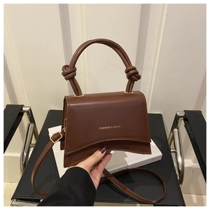 Detail of a brown leather square bag featuring a curved base and knotted handle design