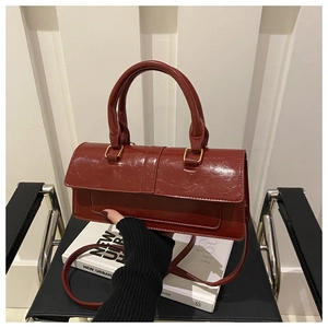 Macro detail of red glossy oil wax leather shoulder bag with gold hardware and top handle