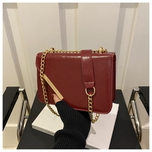 Close-up of glossy deep red chain crossbody bag with golden hardware and leather detail
