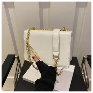 Close-up of a white leather crossbody bag with golden chain and metallic buckle detail