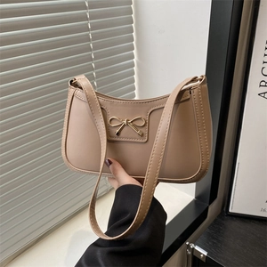 Minimalist beige leather underarm crescent bag with golden bow hardware shown handheld