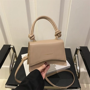 Beige faux leather handbag with knot handle and curved base on a decorative box