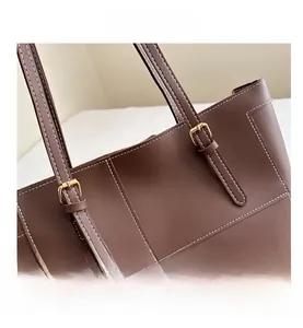 Detailed close-up of brown leather tote with white stitching and gold metal buckle