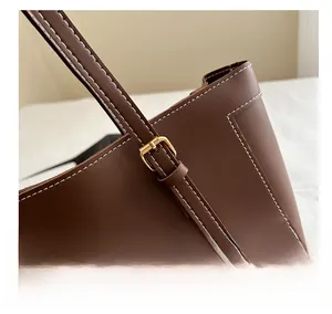 Detail of dark brown leather tote with gold metal buckle and contrast white stitching