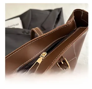 Detail of smooth gold zipper and contrast white stitching on brown leather tote bag