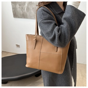 Detail of a brown tote bag with contrast stitching and front pocket on grey coat