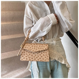 Detail of a beige floral embossed handbag with a unique knotted handle on a model