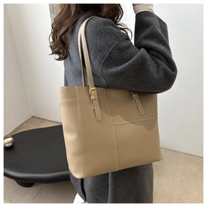 Side view of a khaki leather tote bag worn by a model in a minimalist setting