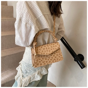Detail of beige faux leather handbag with embossed clover patterns and knot handle