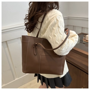 Detail of dark brown tote bag with white contrast stitching and fine leather texture