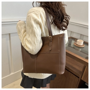 Detail of dark brown tote bag with white contrast stitching and decorative buckle strap