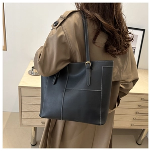 Black leather tote bag with white contrast stitching worn by a model in a cozy interior