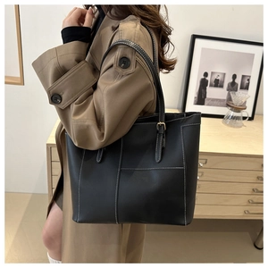 Detail of a black tote bag with white contrast stitching and slim shoulder straps