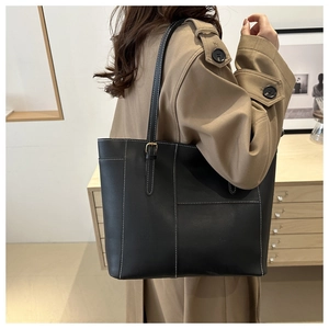 Detail of black tote bag with white contrast stitching and gold buckle on shoulder strap