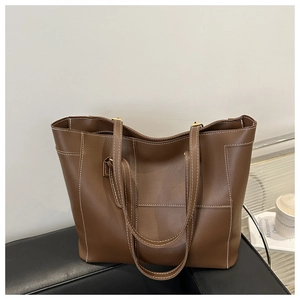 Detail of a large dark brown tote bag with contrast white stitching on a leather sofa