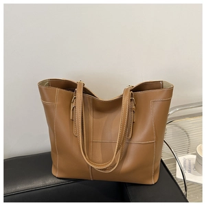 Detail of brown leather tote bag with white contrast stitching and metal buckle handles
