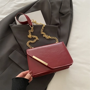 Elegant burgundy chain crossbody bag with gold metal trim on a stylish grey suit