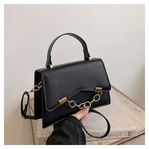Detail of black faux leather handbag with gold chain ornament and V-cut flap design