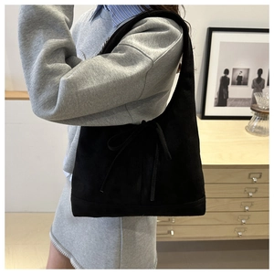 Detail of black suede tote bag with decorative bow and minimalist half-moon underarm shape