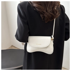 Detail of white crossbody bag with wavy bottom and gold lettering on black blazer