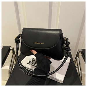 Close-up of black leather shoulder bag with knotted strap and gold fashion lettering