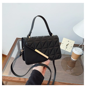 Détail d'un petit sac carré matelassé noir avec boucle dorée et anse élégante portée main