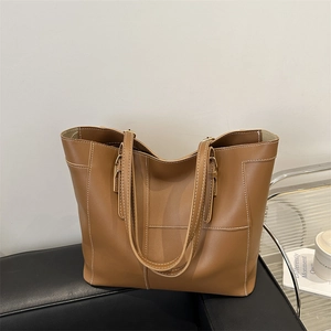 Classic caramel brown tote bag with contrast stitching on a stylish leather sofa