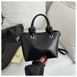 Détail du sac à main en cuir noir avec poignée nouée, anneaux dorés et texte fashion