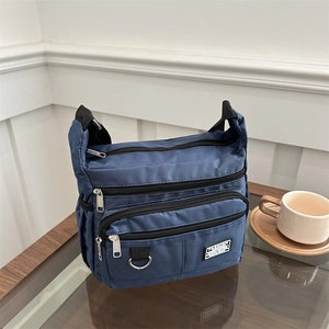 Dunkelblaue Nylon-Umhängetasche mit Reißverschlüssen und Modeschild auf Holztisch
