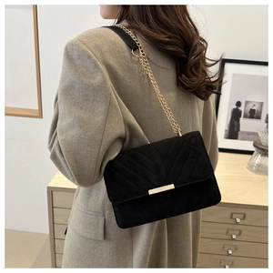 Close-up of black quilted shoulder bag with V-shaped pattern and gold chain strap detail