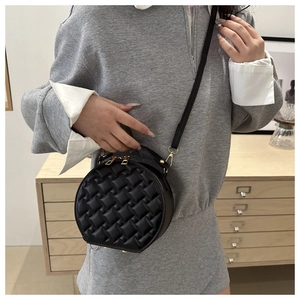 Detail of black quilted round bag featuring gold metal zipper and leather handle