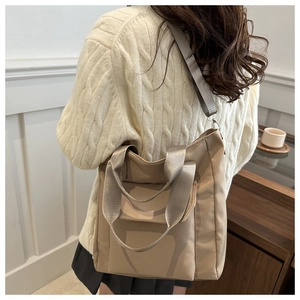Detail view of a beige nylon tote bag worn by a model in a minimalist interior setting